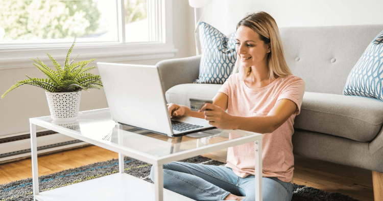 Woman sitting in front of a gray couch using a laptop to manage a line of credit or credit card