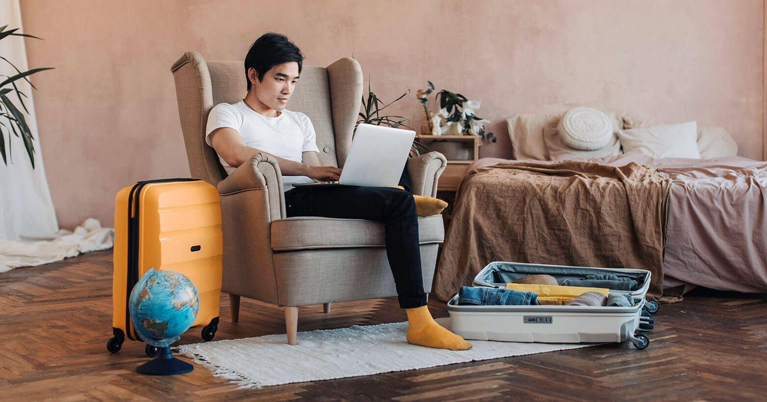 Man sitting in a chair with a laptop surrounded by luggage