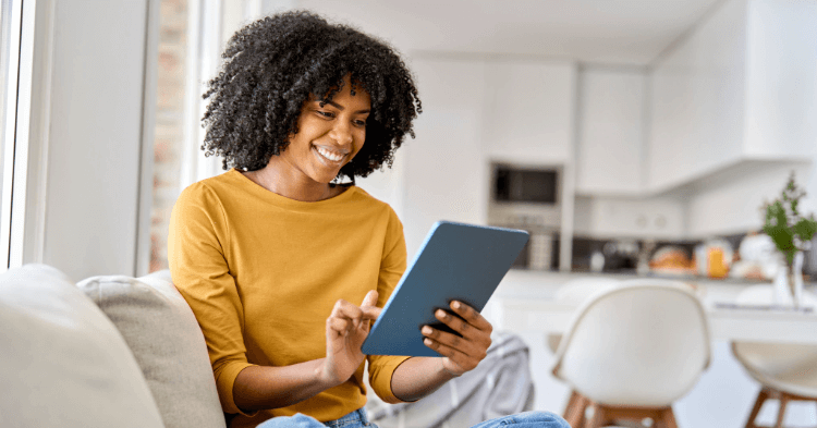 Woman in a yellow sweater sits on her couch looking at a tablet
