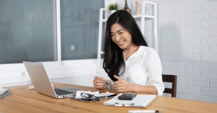 Woman at a table with her laptop, a calculator and papers
