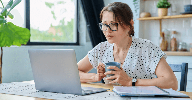 woman at her kitchen table on a laptop with a cup of coffee applying for a personal loan