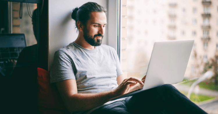 Man sitting in a window sill on his laptop