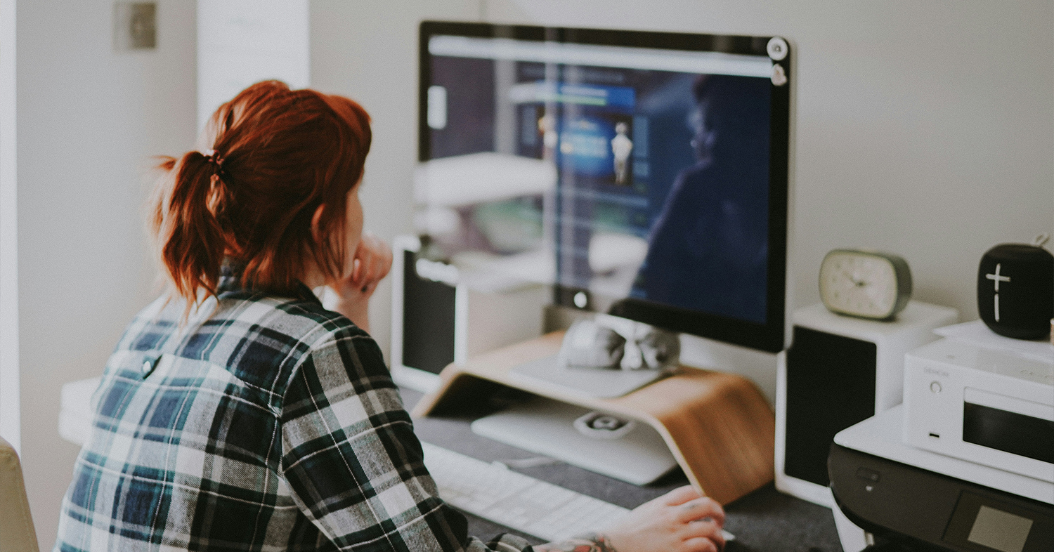 A photo of a person sitting at a desk and looking at a computer screen.