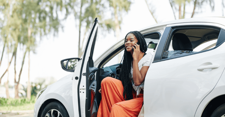 Woman sitting in her car with the door open talking on the phone