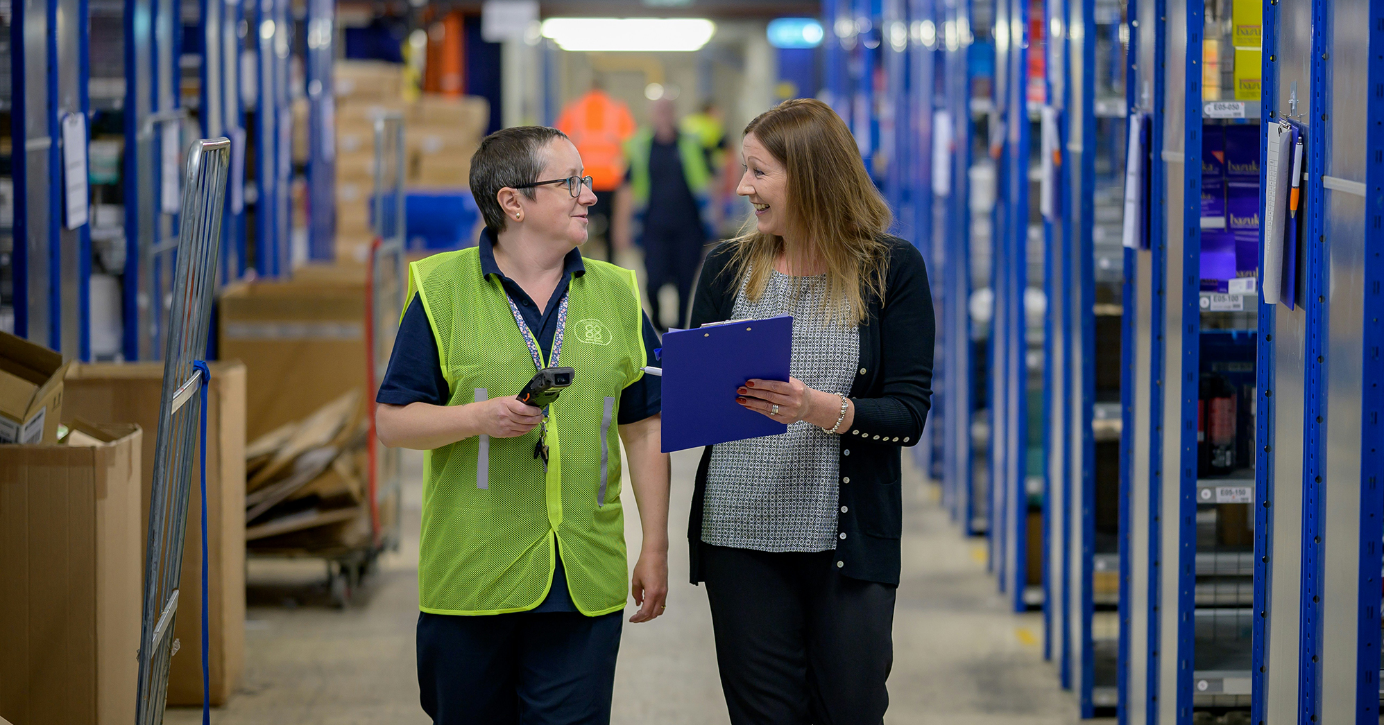 A photo of two workers looking at a clipboard and talking.